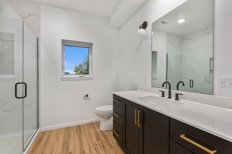 Bright bathroom in Bloomington, IL with dark vanity, gold hardware, glass shower and wood look flooring