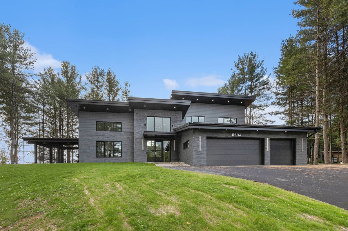Contemporary home in West Michigan with dark exterior, flat roof, and three-car garage, surrounded by tall pine trees