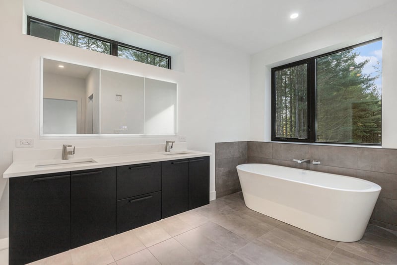 Contemporary primary bathroom with dual vanity and soaking tub by West Michigan custom builder R-Value Homes