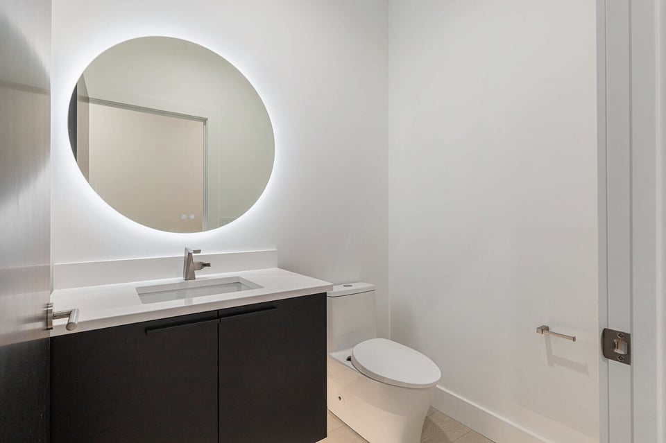 Minimalist powder room in West Michigan with backlit mirror and black vanity, remodeled by R-Value