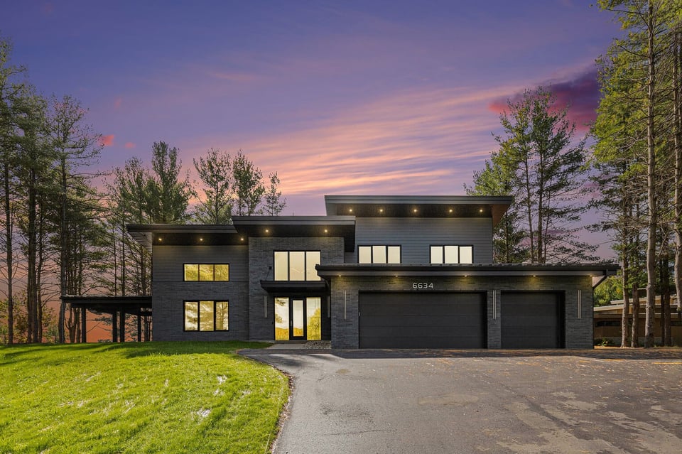 Modern West Michigan home lit up at sunset, showcasing large windows, flat rooflines, and sleek architectural lines