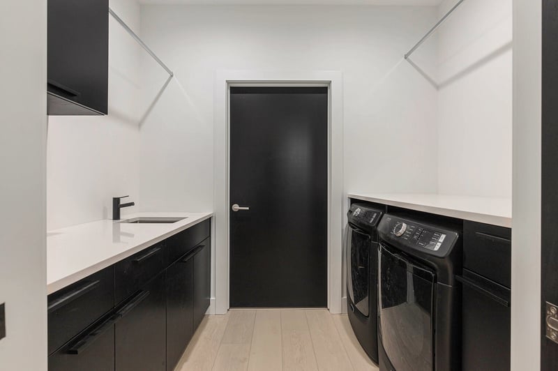 Modern laundry room in West Michigan with black cabinetry, quartz counters, and washerdryer installed by R-Value Homes