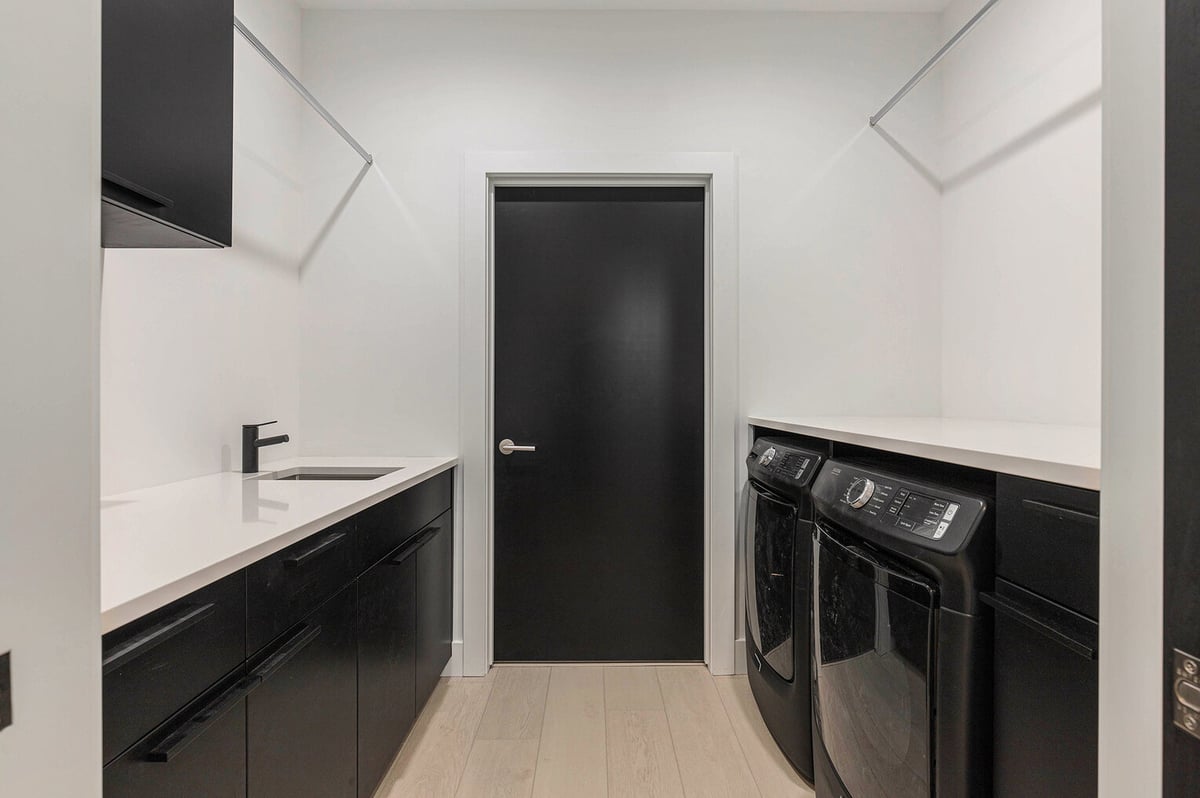 Modern laundry room in West Michigan with black cabinetry, quartz counters, and washerdryer installed by R-Value Homes