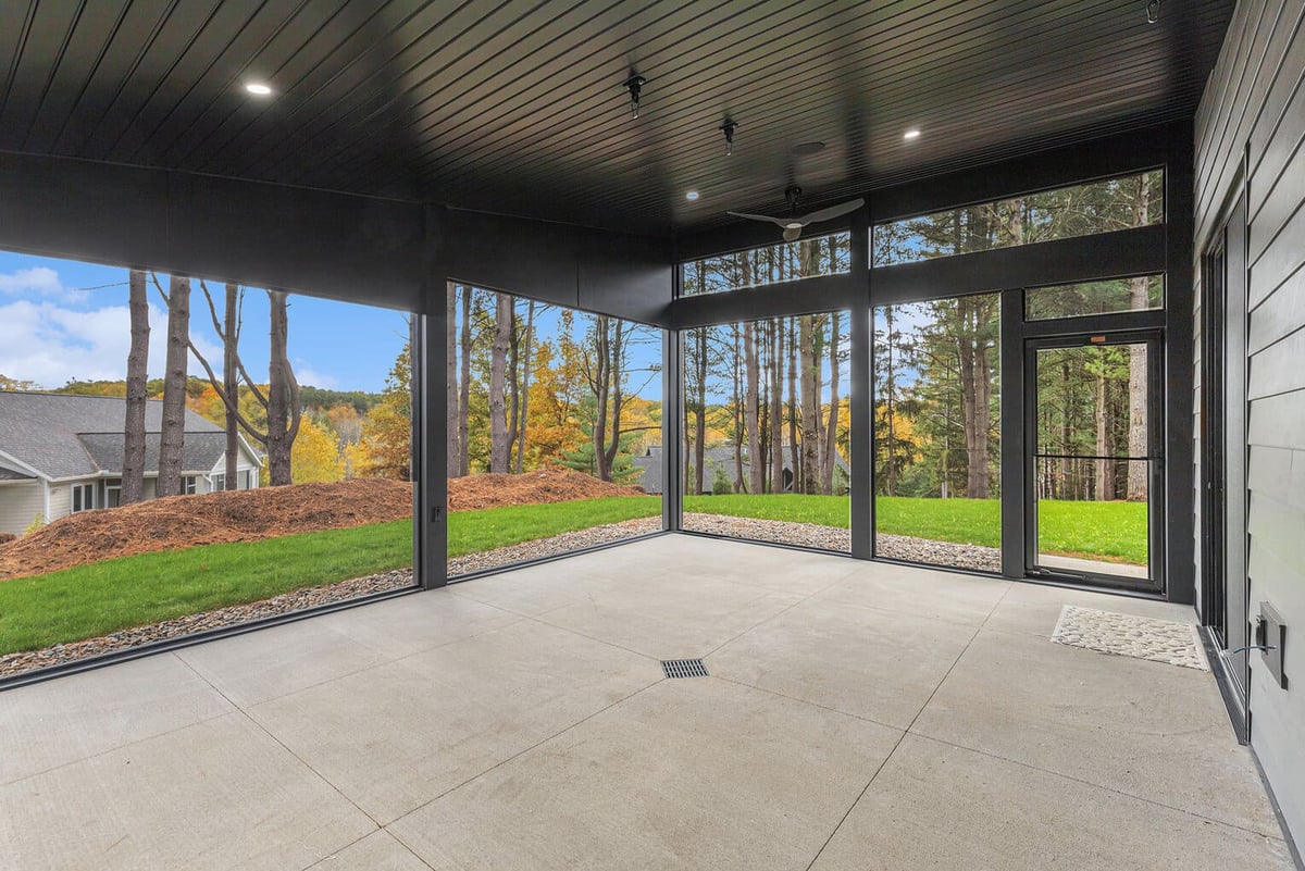 Modern screened-in patio in a new West Michigan home with forest views and sleek black trim