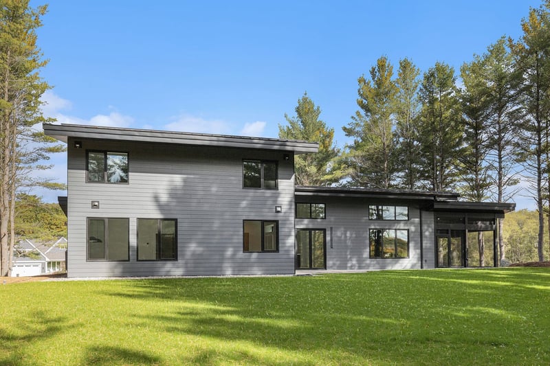 Rear exterior of a contemporary West Michigan home with large windows and surrounded by mature pines