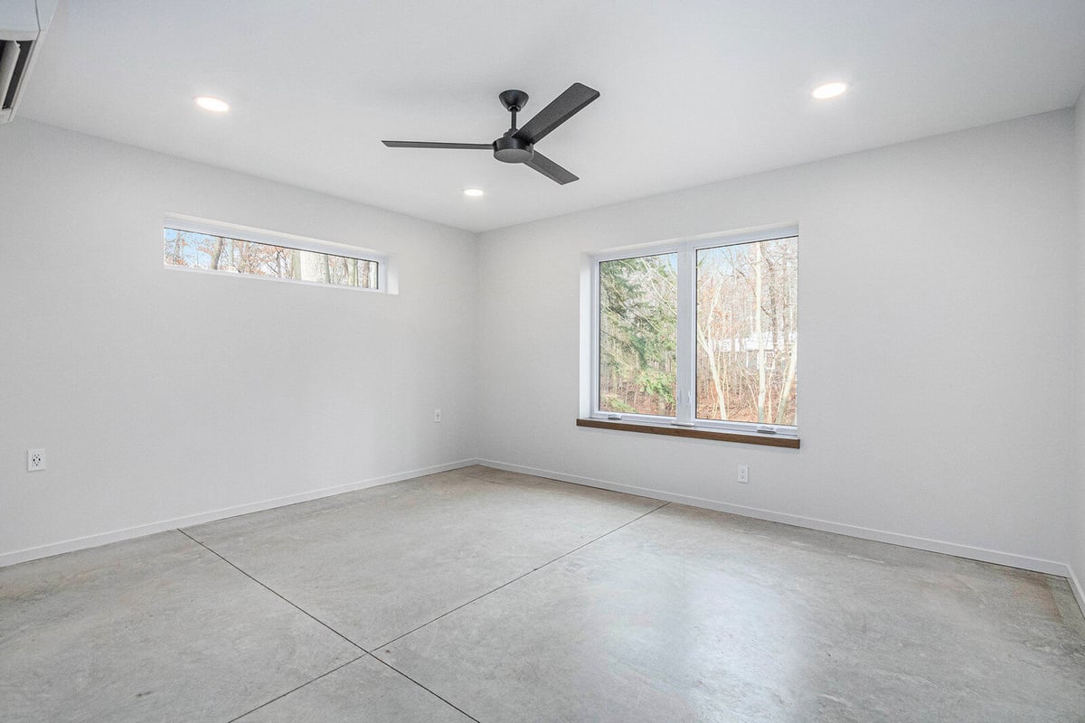 Minimalist bedroom with large windows and ceiling fan, part of a West Michigan custom home by R Value Homes