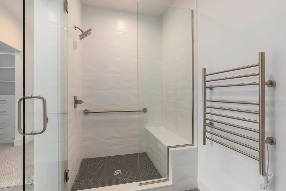 Primary bathroom tiled shower with bench and towel warmer in a custom home built by R-Value Homes in West Michigan