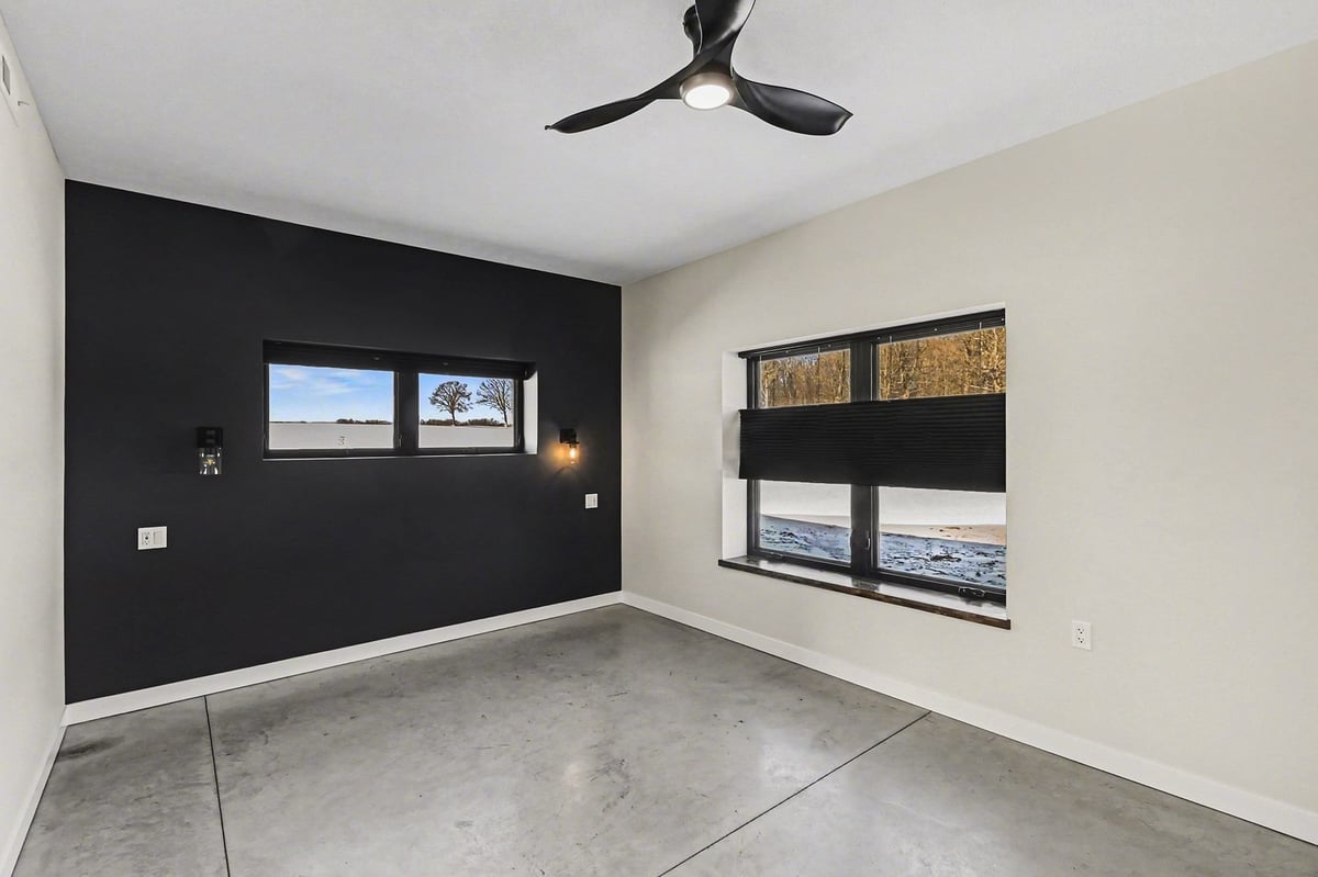 Primary bedroom with modern ceiling fan and dark accent wall in a custom home in West Michigan