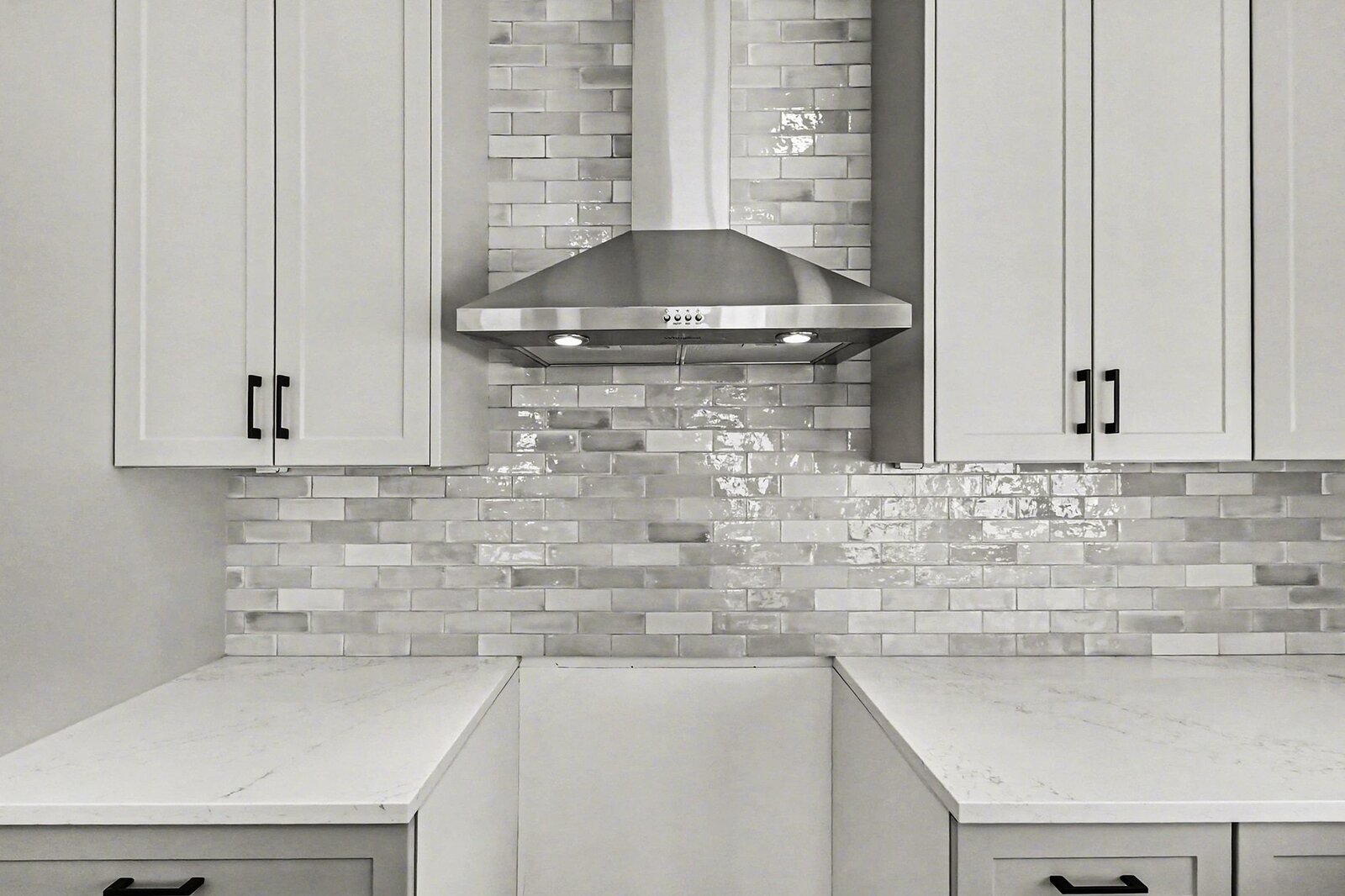 Close-up of modern kitchen range hood with white cabinetry and gray tile backsplash in a Western Michigan home