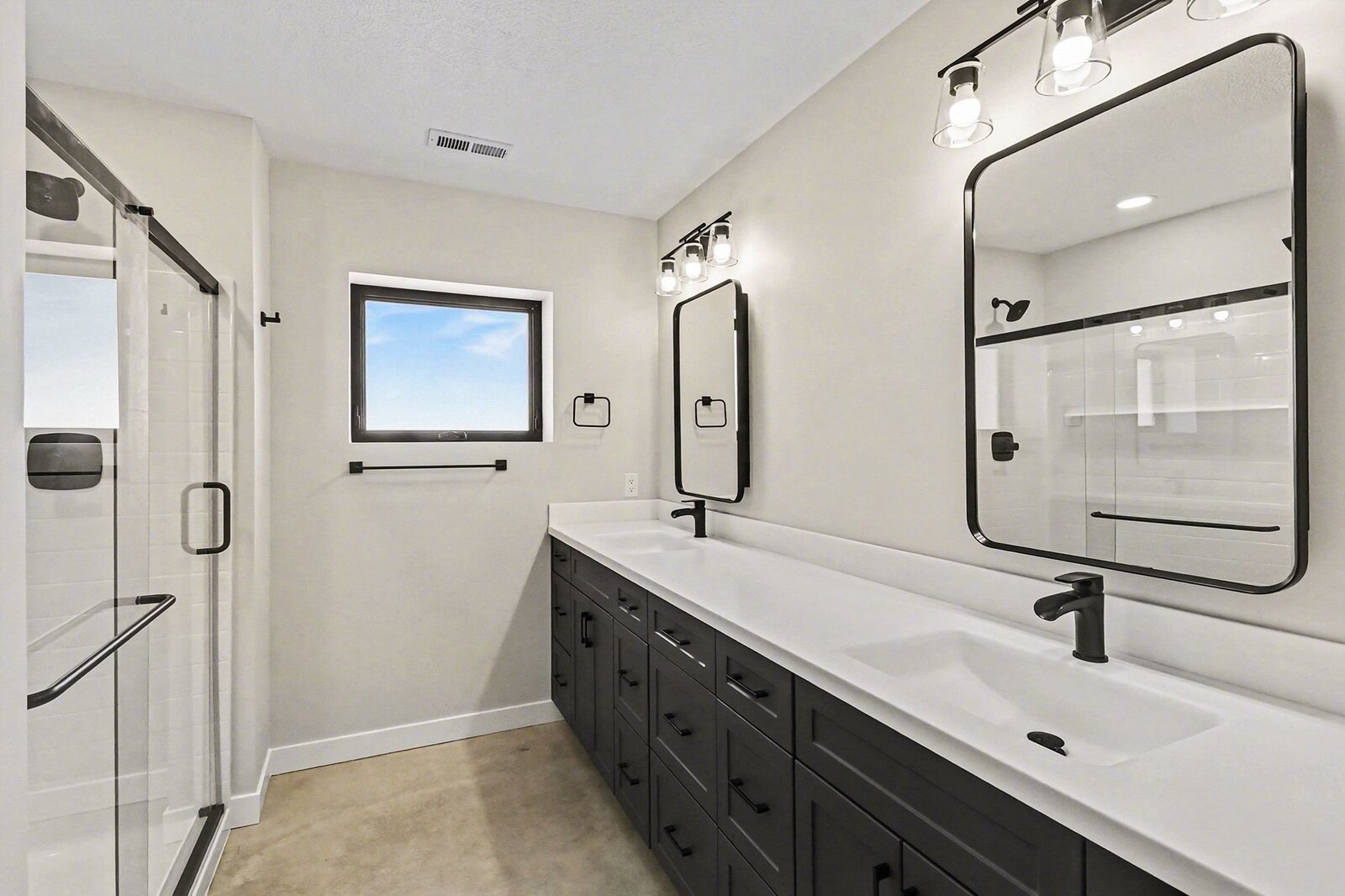 Modern bathroom in a Western Michigan home with double vanity, black fixtures, large mirrors, and glass walk-in shower