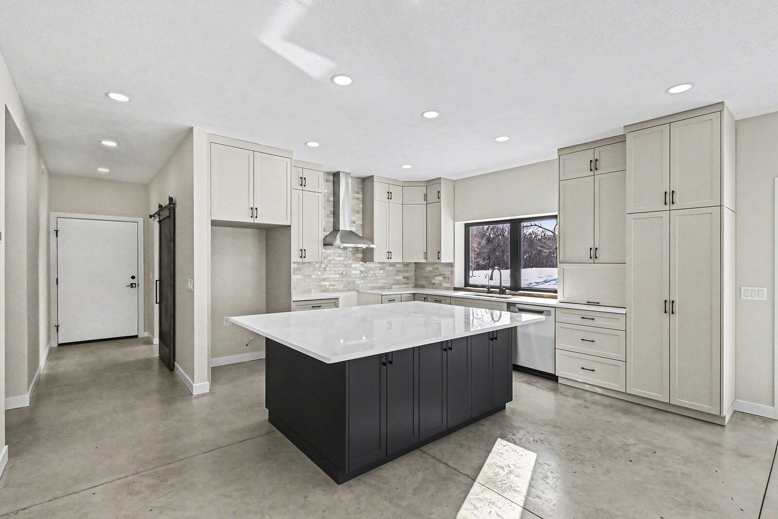 Modern kitchen in a Western Michigan home with large white island, light cabinetry, tile backsplash, and concrete floors