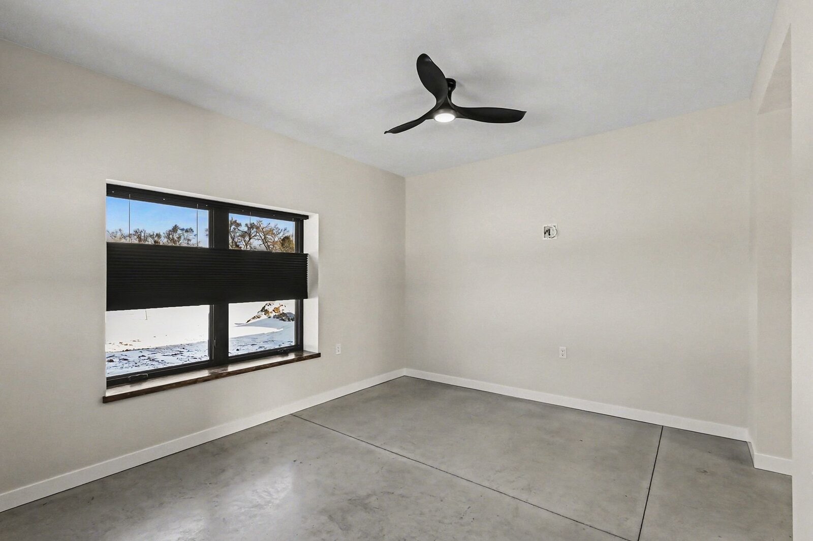 Spacious bedroom in a Western Michigan home with concrete floors, ceiling fan, and large window overlooking snowy fields