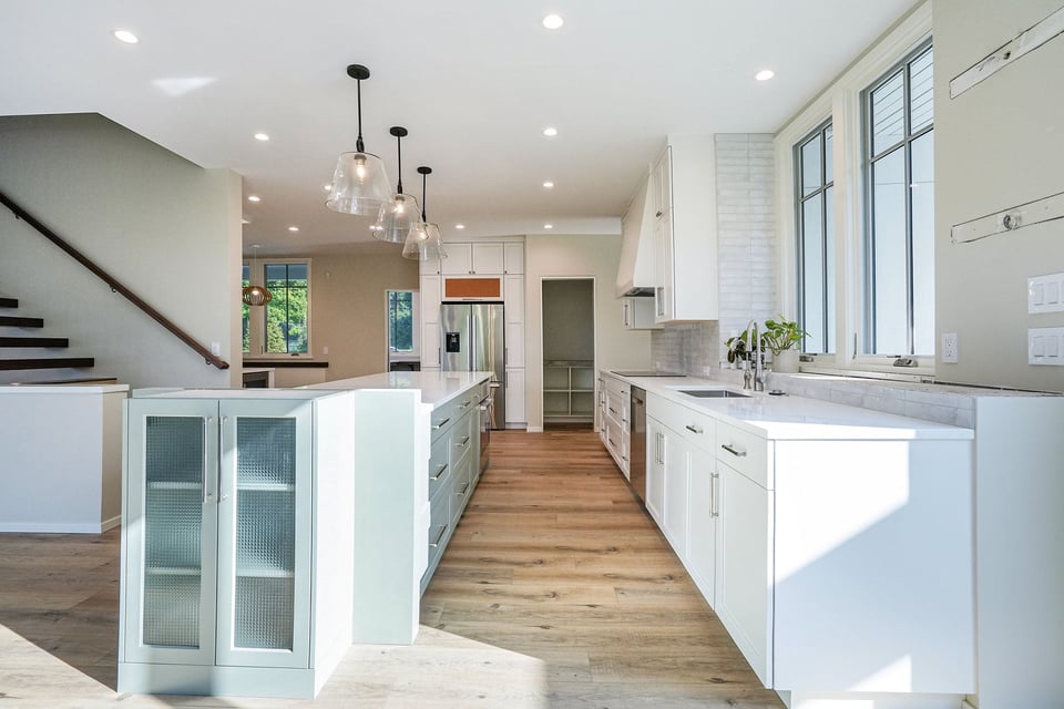 Spacious modern kitchen in West Michigan featuring white cabinetry, wood floors, pendant lighting, and large island
