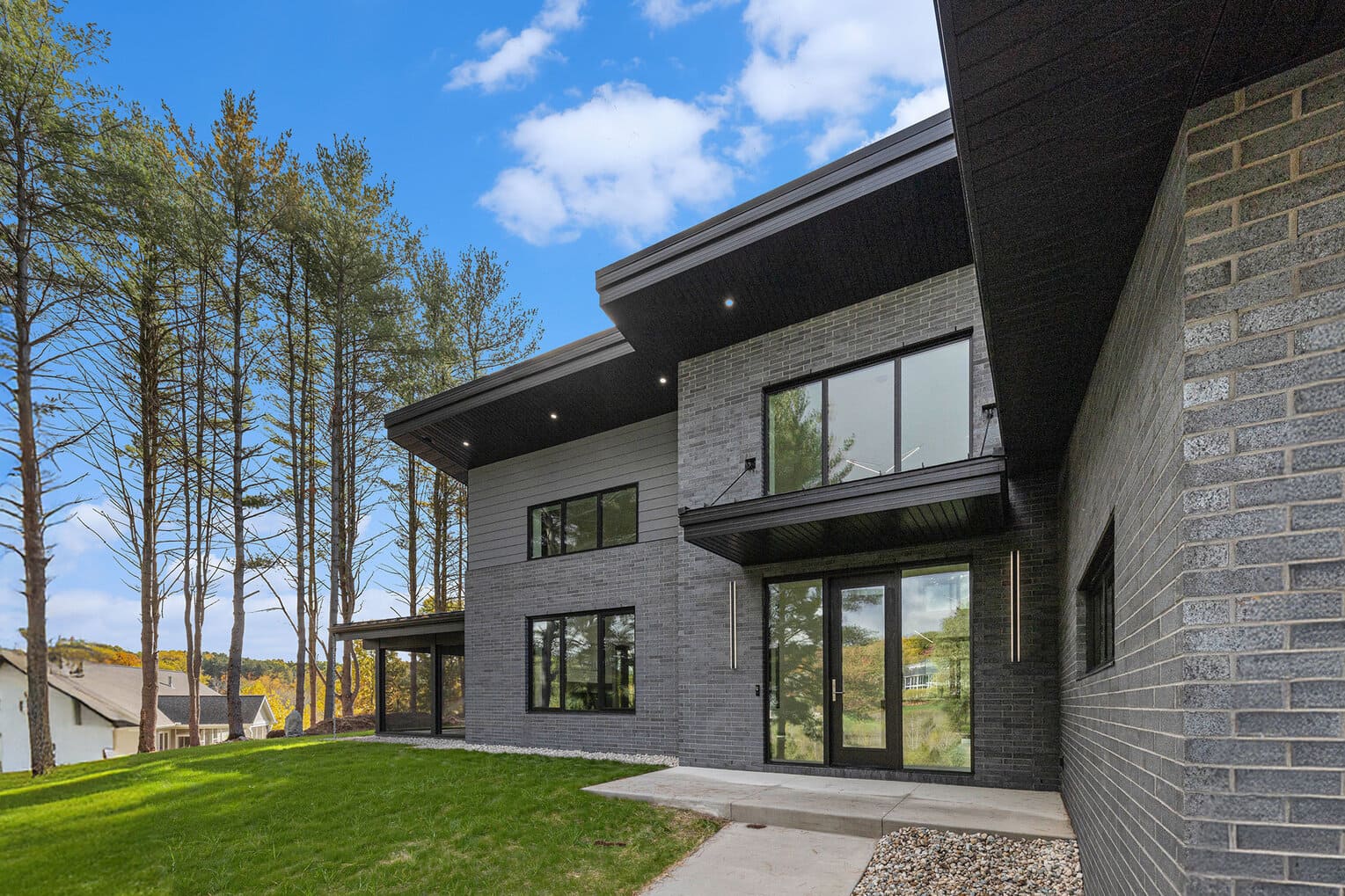 Side view of a dark gray modern West Michigan home with large windows and sloped roof, surrounded by forested greenery