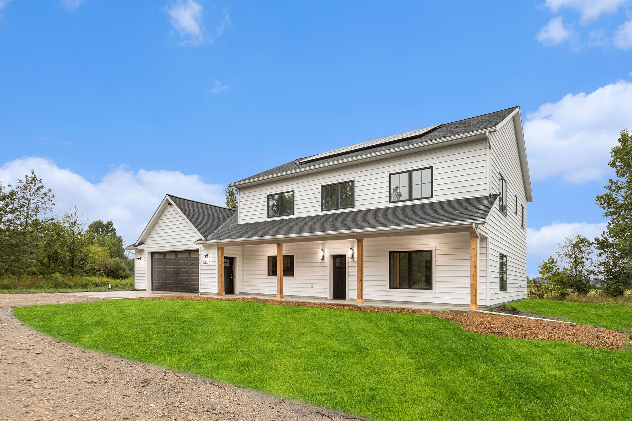 Modern white farmhouse-style home with black trim, large windows, and attached garage located in West Michigan