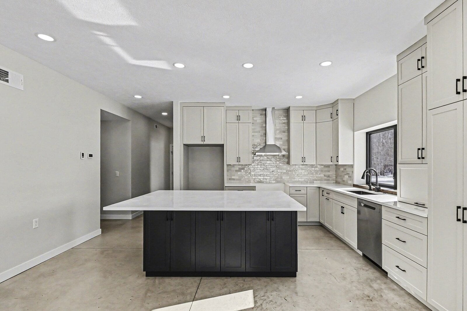 Bright modern kitchen in Western Michigan with large island, white cabinets, stainless hood, and window overlooking snowy landscape