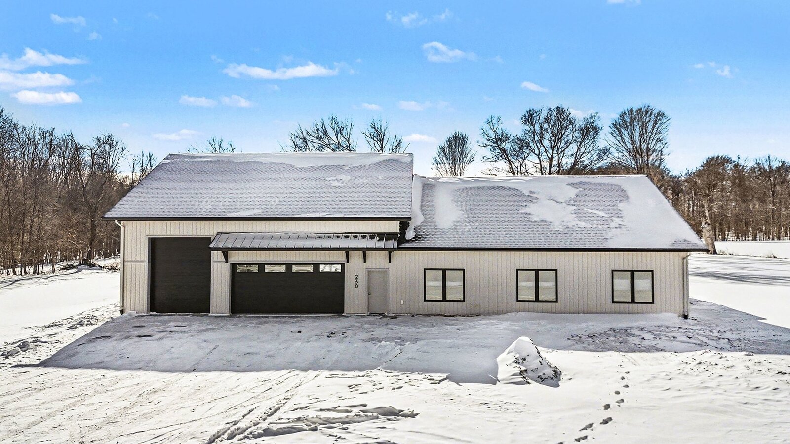 Modern barn-style home with black garage doors and metal awning surrounded by snow-covered fields under a bright winter sky in Western Michigan
