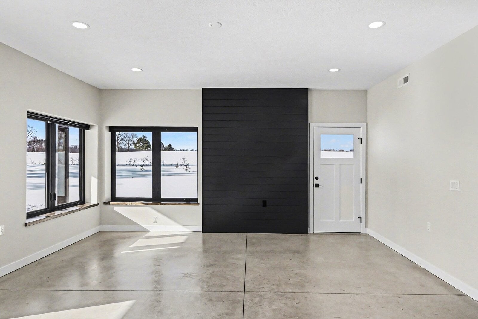 Open living space in a Western Michigan home with large windows overlooking snowy fields, black accent wall, and polished concrete floors