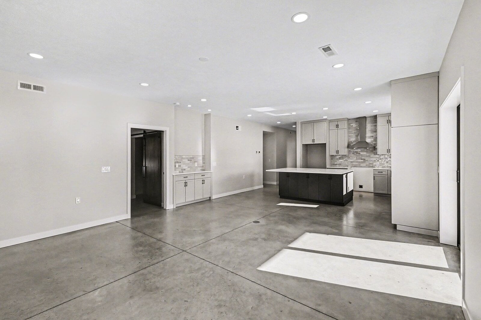 Open-concept living area and kitchen with large island, white cabinetry, and polished concrete floors in a modern Western Michigan home