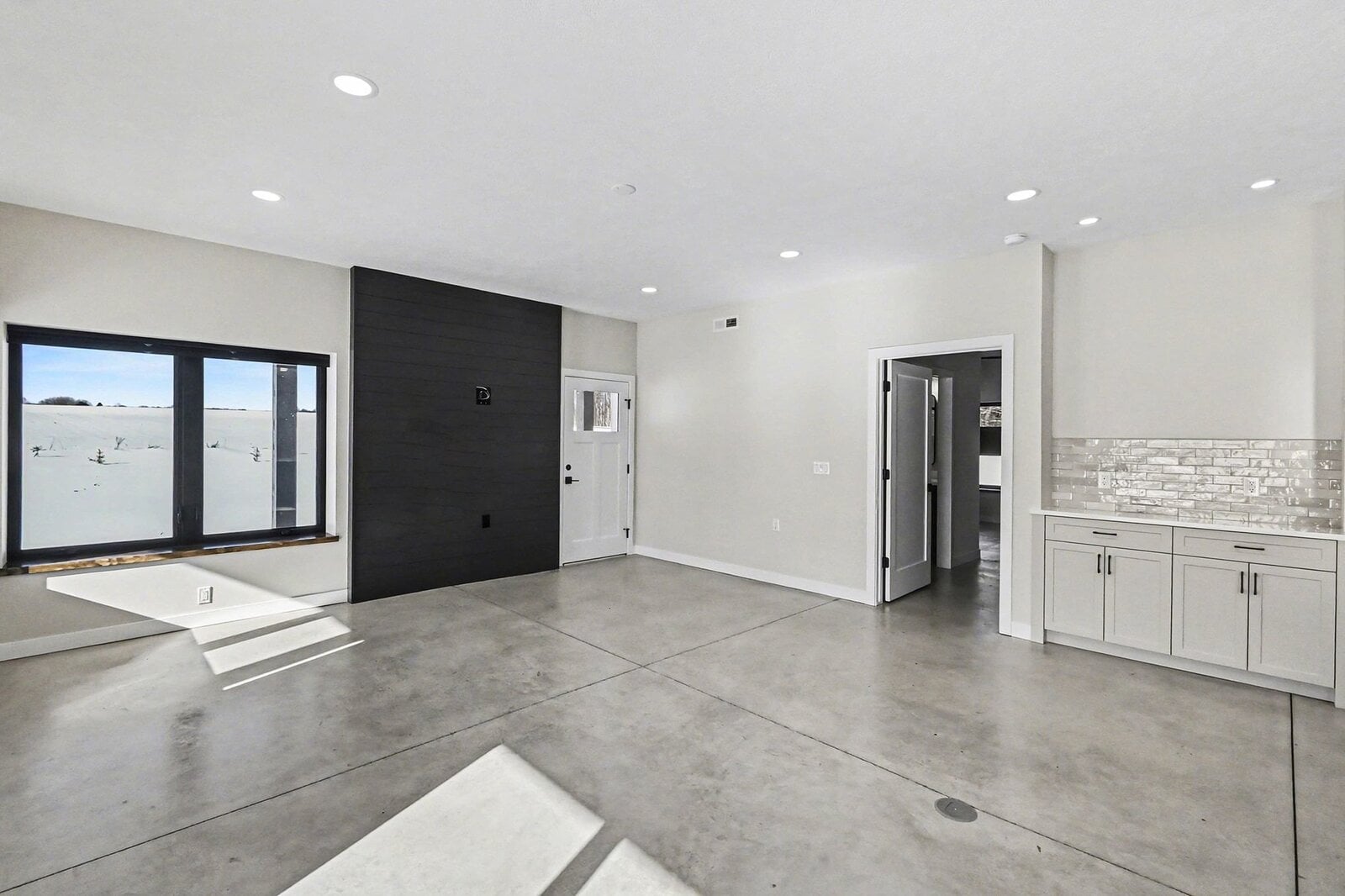 Spacious living area in a Western Michigan home with polished concrete floors, large window views of snowy fields, and built-in cabinetry